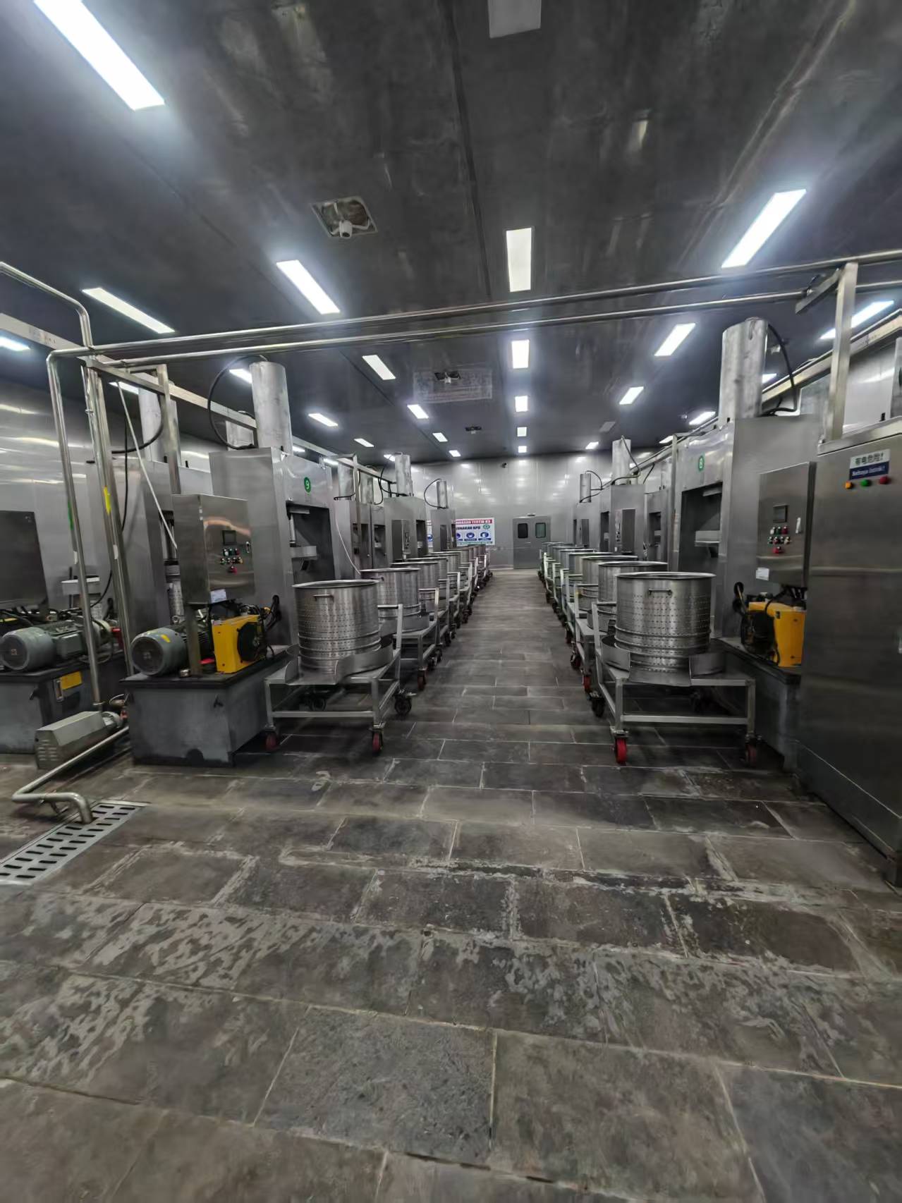 Factory production floor with automated pressing equipment and stainless steel processing tanks